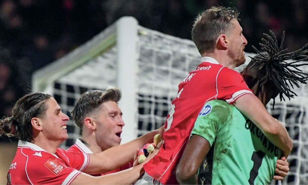 Wrexham players mob keeper Arthur Okonkwo after his penalty heroics