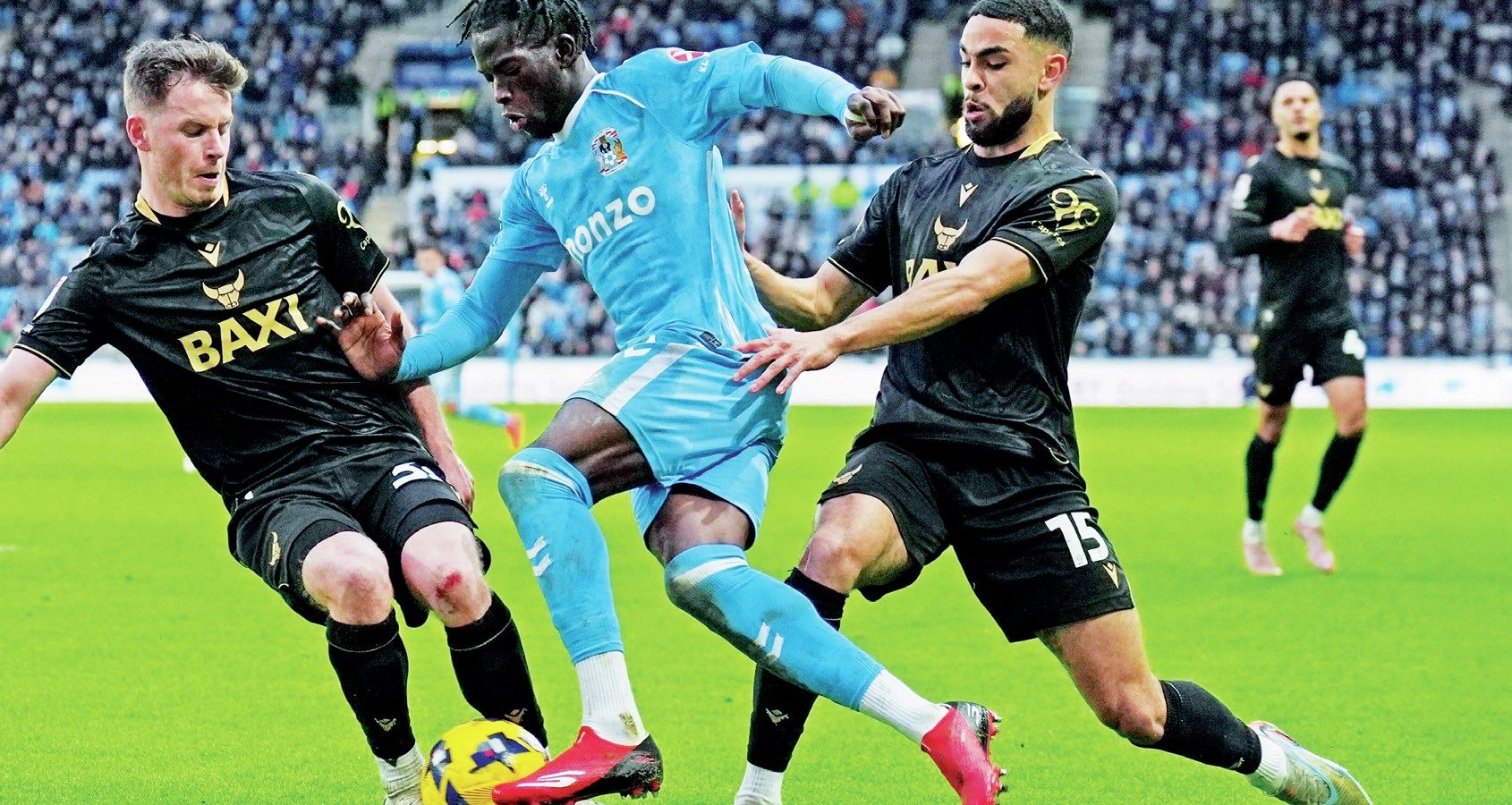 Coventry City attacker Romain Esse is challenged by Oxford United’s Jamie McDonnell, left, and Brodie Spencer